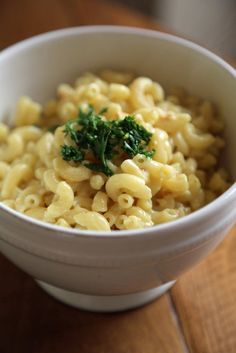 a white bowl filled with macaroni and cheese covered in parsley on top of a wooden table