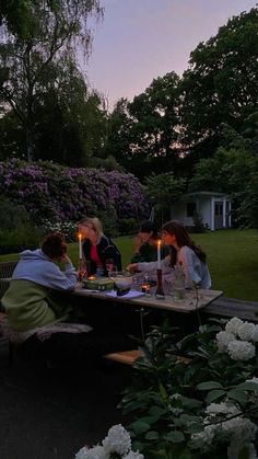 four people sitting at a table with candles in their hands and flowers on the ground