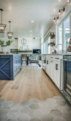 an open kitchen with white cabinets and blue island in the center, surrounded by wood flooring