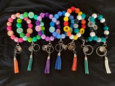 several different colored beads and tassels on a black cloth covered surface with keychains