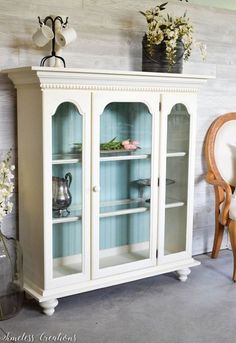 a white china cabinet with glass doors and flowers on top