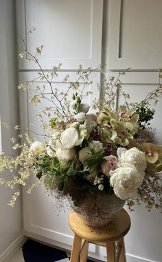 a vase filled with lots of flowers sitting on top of a stool next to a door