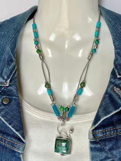 Brilliant Malachite/Chrysocolla pendant in 925 silver, mated with Blue Agate, Jade, Chrysocolla and Silver Alloy beads on two strands of 1mm metallic silver leather cording. Silver toggle to close. Pendant is 2" long total and stone is 3/4"x3/4". Length of necklace is 20" and 22" with pendant. SIDE NOTE: Pendant was created by another Artisan whose work I admire and enjoying embellishing. No nickel or lead used. Please use the Last On, First Off approach. Stones discolor with lotions, perfumes, hairspray, sweat, chlorine, even some soaps, and will break if dropped. Silver Chrysocolla Jewelry With Gemstone Beads, Unique Green Chrysocolla Necklaces, Nickel-free Green Chrysocolla Jewelry, Adjustable Size Green Turquoise Necklace In Sterling Silver, Turquoise Necklace For Jewelry Making With Chrysocolla, Adjustable Green Turquoise Necklace In Sterling Silver, Chrysocolla Turquoise Necklace For Jewelry Making, Artisan Necklace, Blue Agate