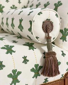 an upholstered bed with green and white wallpaper, tasseled cushions and wooden headboard