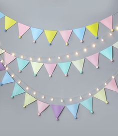 multicolored bunting flags with lights strung from them on a gray wall background