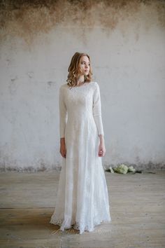 a woman wearing a white dress standing in front of a wall and looking off to the side