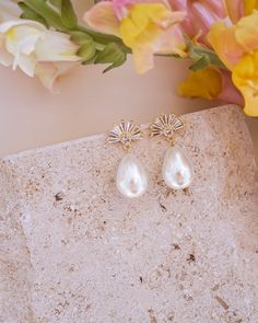 two pairs of pearl earrings sitting on top of a stone slab with flowers in the background