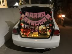 the trunk of a white car is decorated with pink and red happy birthday banners, lights, and decorations