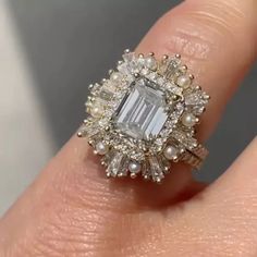 a close up of a person's hand wearing a ring with an emerald and white diamond