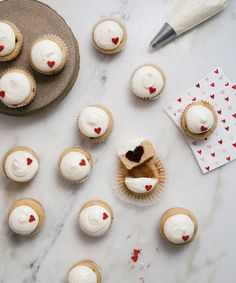 cupcakes with white frosting and red hearts on them next to a plate