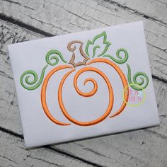 an embroidered applique pumpkin with swirls and leaves on white fabric sitting on a wooden surface