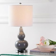 a glass table topped with a lamp next to a bowl of flowers and a book