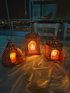 three lit candles sitting on top of a table next to each other in front of a window