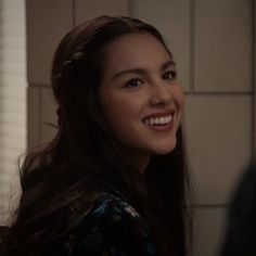 a woman with long brown hair smiling at someone in the background and wearing a floral shirt