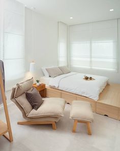 a bed sitting next to a chair and ottoman in a room with white walls on the other side