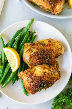 two plates with chicken, green beans and lemon wedges on them next to some parsley