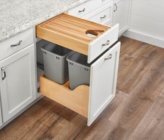 an open cabinet with two trash cans and a cutting board in the bottom drawer is shown