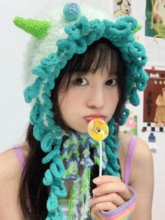 a young woman wearing a crocheted hat and holding a lollipop