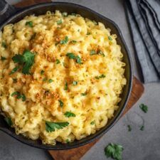 a bowl filled with macaroni and cheese on top of a wooden cutting board