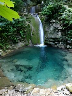 there is a small waterfall in the middle of this pool with blue water and rocks