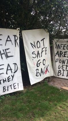 three signs with words written on them in front of a tree and grass covered yard