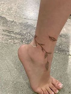 a woman's foot with a small tattoo on her left ankle and leaves attached to it