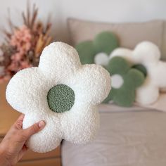 a person holding up a white and green flower shaped pillow in front of a couch