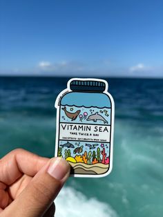 a hand holding up a sticker with the words vitamin sea in front of an ocean view