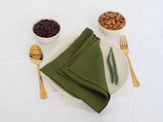 a white plate topped with green napkins next to two bowls filled with beans and nuts