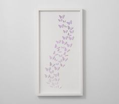 a white frame with purple butterflies hanging on it's wall next to a bed