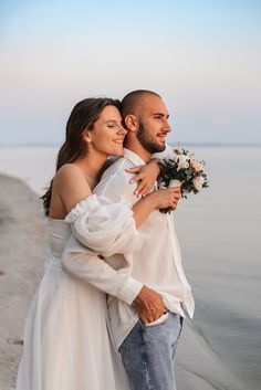 a man and woman hugging each other on the beach with water in the back ground