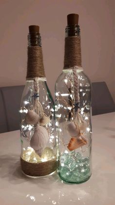 two bottles with seashells in them are sitting on a table together, one is filled with water and the other has lights