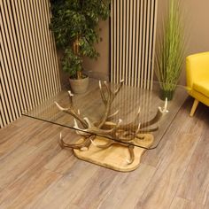 a glass table with antlers on it in front of a yellow chair and potted plant