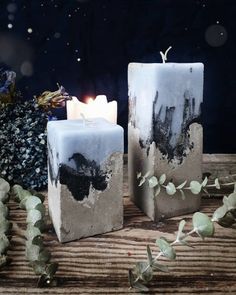 two white candles sitting next to each other on top of a wooden table covered in leaves