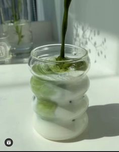 a vase filled with water and cucumbers on top of a white table next to a window