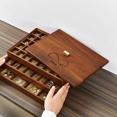 a wooden box with jewelry in it and someone's hand reaching for the lid