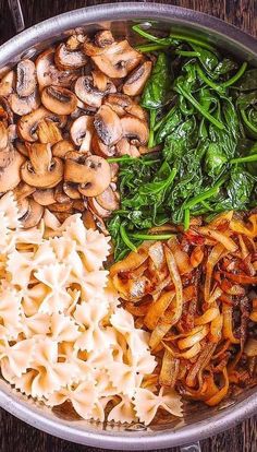 pasta, mushrooms and spinach in a pan on a wooden table