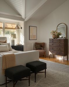 a bed room with a neatly made bed next to a dresser and two stools