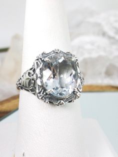 Oval Gem Sterling Silver Filigree RingBeauty Design#D229 Introducing the magnificent D229 Beauty Ring, a brand-new Vintage reproduction sterling silver filigree ring. The perfect oval-cut natural gemstone is a jaw-dropping sight. The gemstone is 12mm by 10mm (just shy of 3/8" inch) in size, while the ring itself is 5/8th of an inch (16.5mm) in length and sits 7mm off the finger. This exquisite rendition of a vintage design filigree ring is one of a kind and is sure to make heads turn when you wa Collectible Oval Rings With Gemstone Accents, White Topaz Rings With Gemstone Accents For Gift, Gift Rings With White Topaz And Gemstone Accents, Classic Silver Topaz Ring With Gemstone Accents, Oval Large Stone Moonstone Wedding Ring, Heirloom White Topaz Ring As A Gift, Heirloom White Topaz Ring For Gift, Heirloom White Topaz Ring As Gift, Heirloom White Topaz Ring Gift