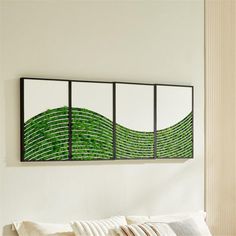 a white bed topped with pillows next to a wall mounted art piece on the wall