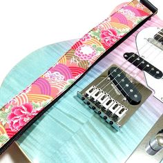 an electric guitar strap with colorful flowers on the top and bottom, along with two guitars