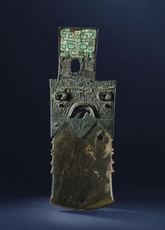 an old bronze object with green and blue designs on it's face, against a dark background