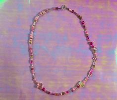 a necklace with pink and yellow beads on a purple tableclothed surface in front of a light green background