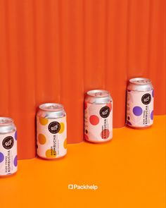 four cans of soda are lined up against an orange wall with polka dots on it