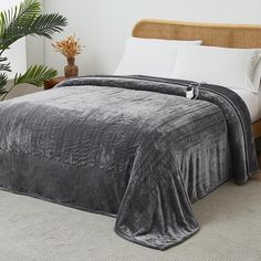 a bed covered in a gray blanket next to a potted plant