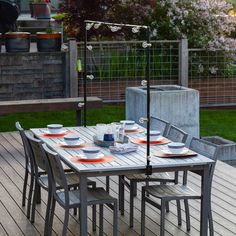 an outdoor dining table set up with plates and cups on it, in the middle of a deck