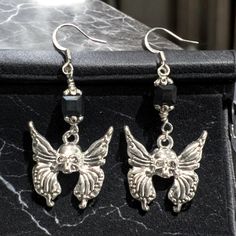 Elevate Your Gothic Style With These Striking Butterfly Skull Earrings. Crafted In Silver-Tone Metal, The Earrings Feature Intricately Designed Wings Framing A Detailed Skull At The Center. The Addition Of Faceted, Black Iridescent Square Beads Adds A Dimensional And Mysterious Allure, Perfect For Anyone Drawn To Edgy, Bold Accessories. These Earrings Blend The Ethereal With The Macabre, Offering A Unique Statement Piece For Any Alternative Wardrobe. Gothic Butterfly, Butterfly Skull, Black Iridescent, Square Beads, Bold Accessories, Skull Earrings, Square Bead, Gothic Style, Gothic Fashion