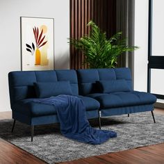 a blue couch sitting on top of a wooden floor next to a plant in a living room