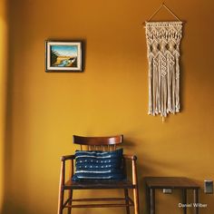 a wooden chair sitting next to a wall with a macrame hanging on it