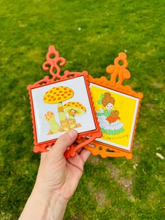 someone is holding up two cards with pictures on them in front of some green grass